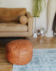 Brown leather ottoman in a living room setting with a beige sofa and on a blue rug