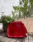 Red leather bag on a wooden deck with plants in the background