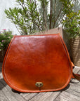 Brown leather bag on a wooden surface with plants in the background