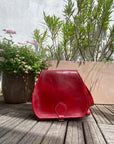 Red leather bag on a wooden surface with plants in the background