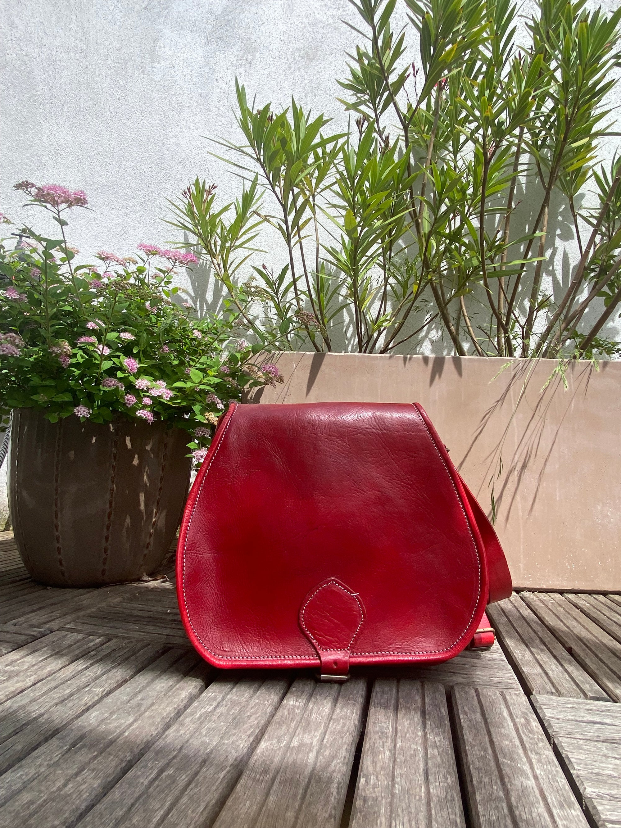 Red leather bag on a wooden surface with plants in the background