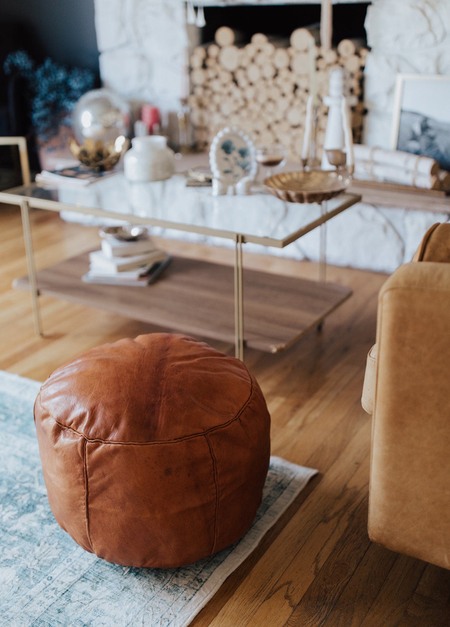 Brown leather ottoman in a living room with a fireplace and marble coffee table.