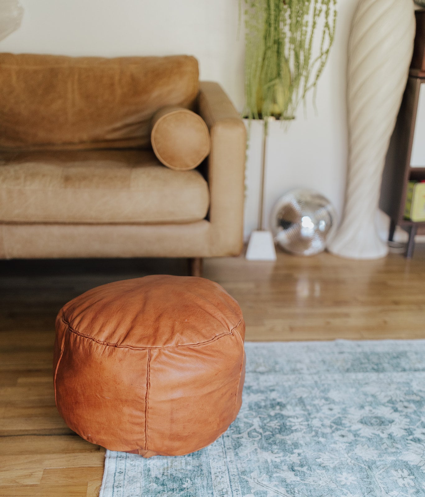 Brown leather ottoman in a living room setting with a beige sofa and on a blue rug