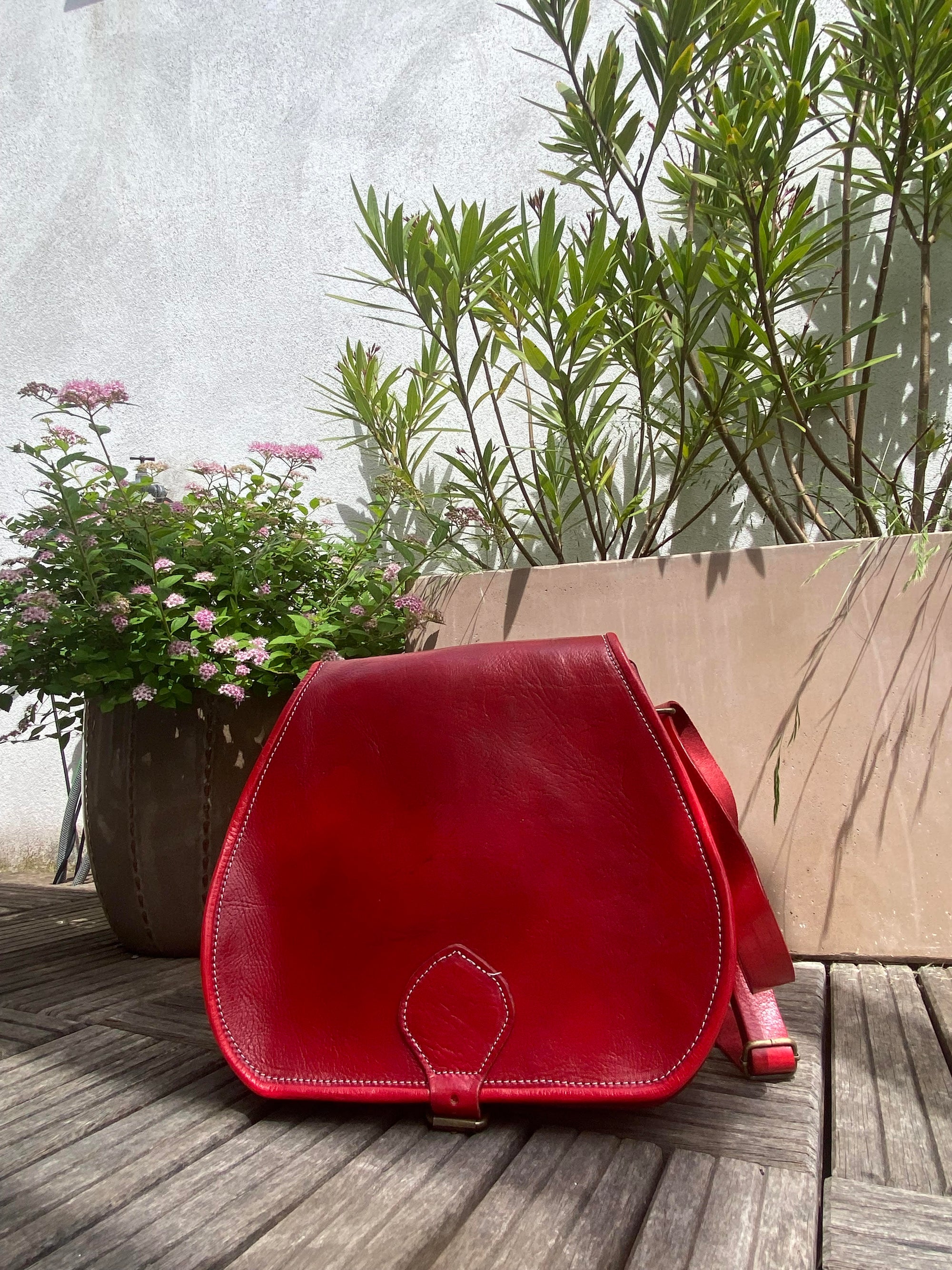 Red leather bag on a wooden deck with plants in the background